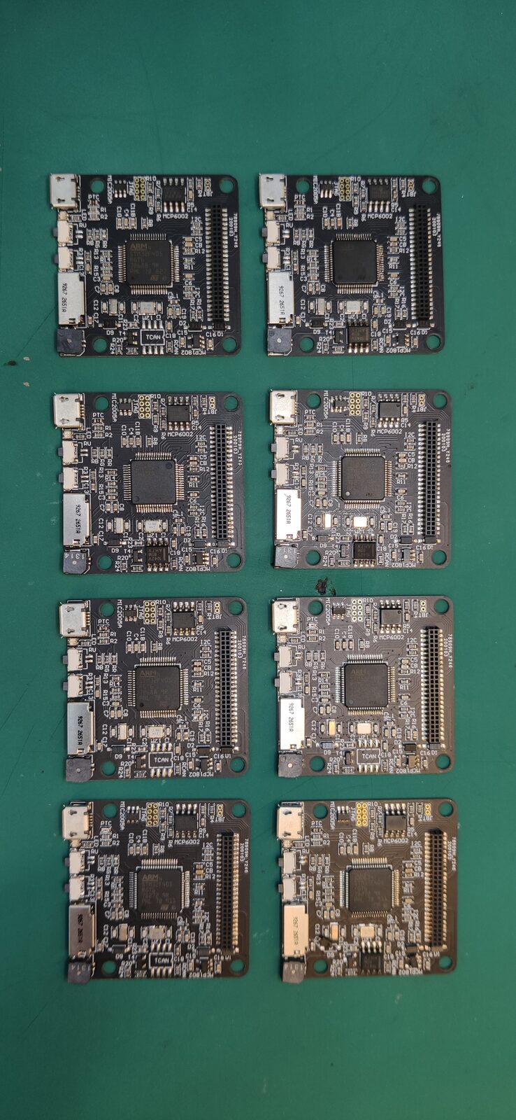 Eight black circuit boards arranged in two columns on a green cutting mat.