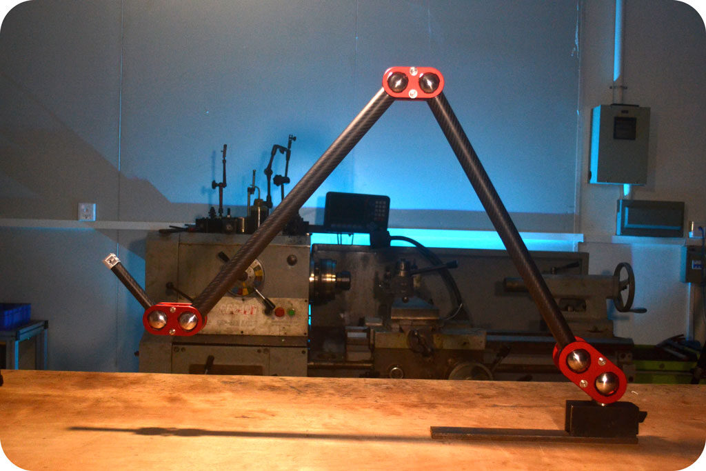 Two-link arm with red joints and black tubes standing on a workbench in front of a lathe, lit with a blue background glow.