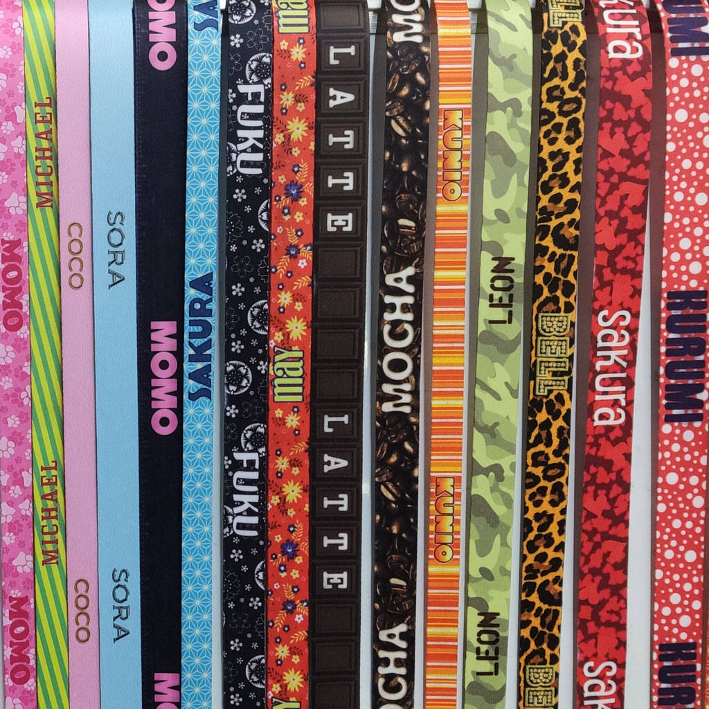 A wall of many leash straps in different colours and patterns, each printed with a dog's name.