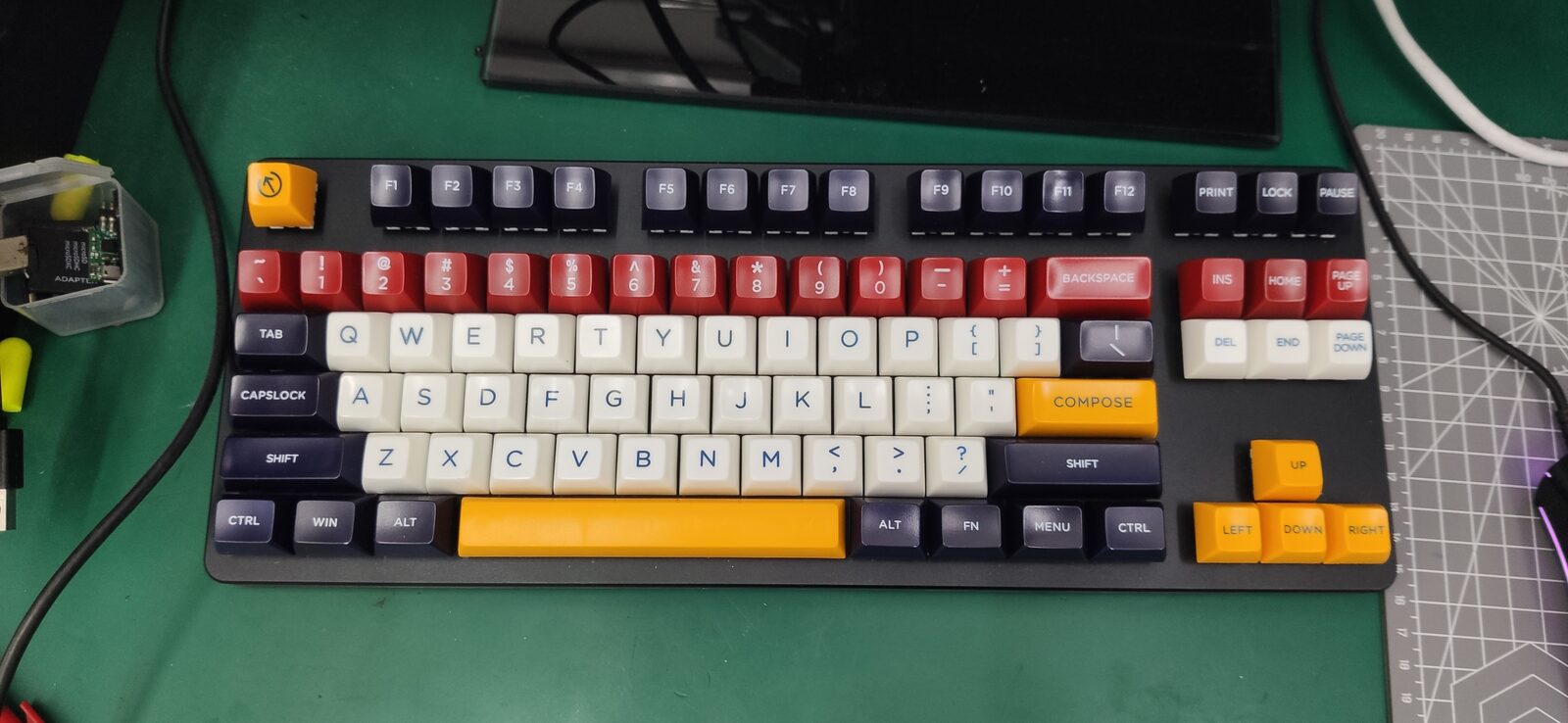 Top view of a compact keyboard with red, white, navy and orange keycaps on a green cutting mat.