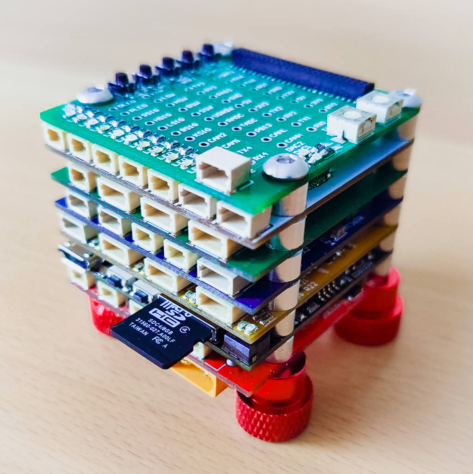 A stack of small green circuit boards with white connector sockets, a microSD card and red knurled feet, photographed on a table.